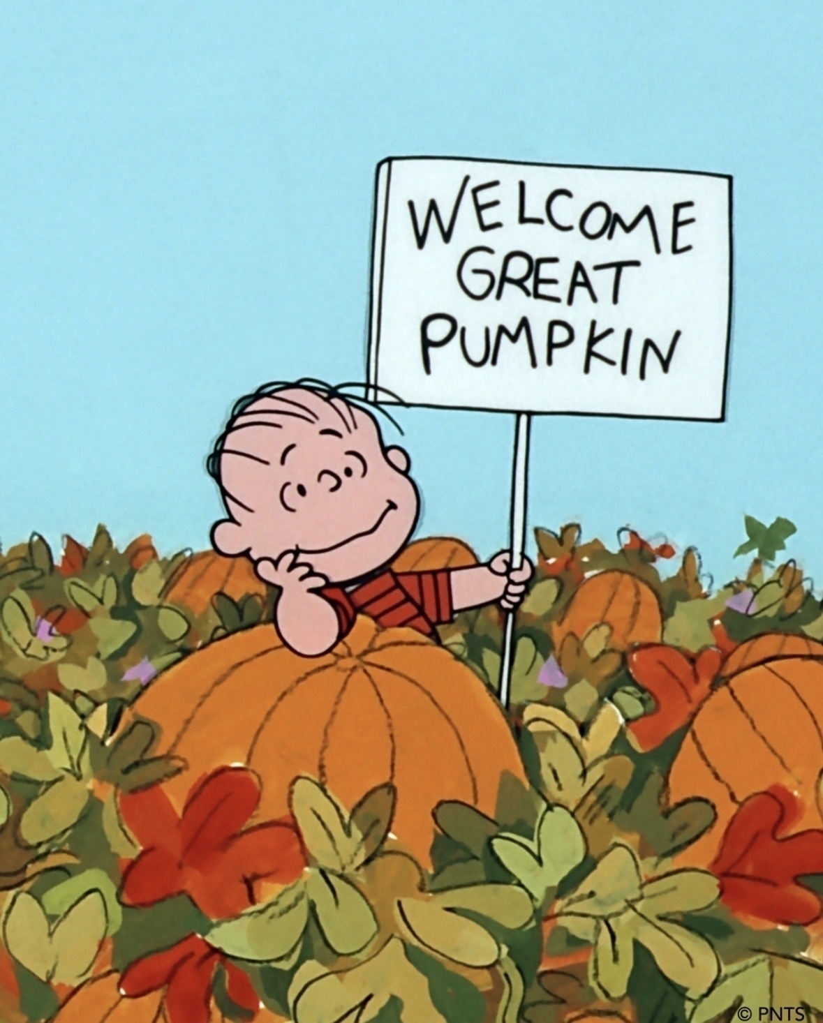 Linus stands by a large pumpkin in a pumpkin patch. He’s leaning in the pumpkin with a dreamy look on his face, holding a sign that reads “Welcome Great Pumpkin”