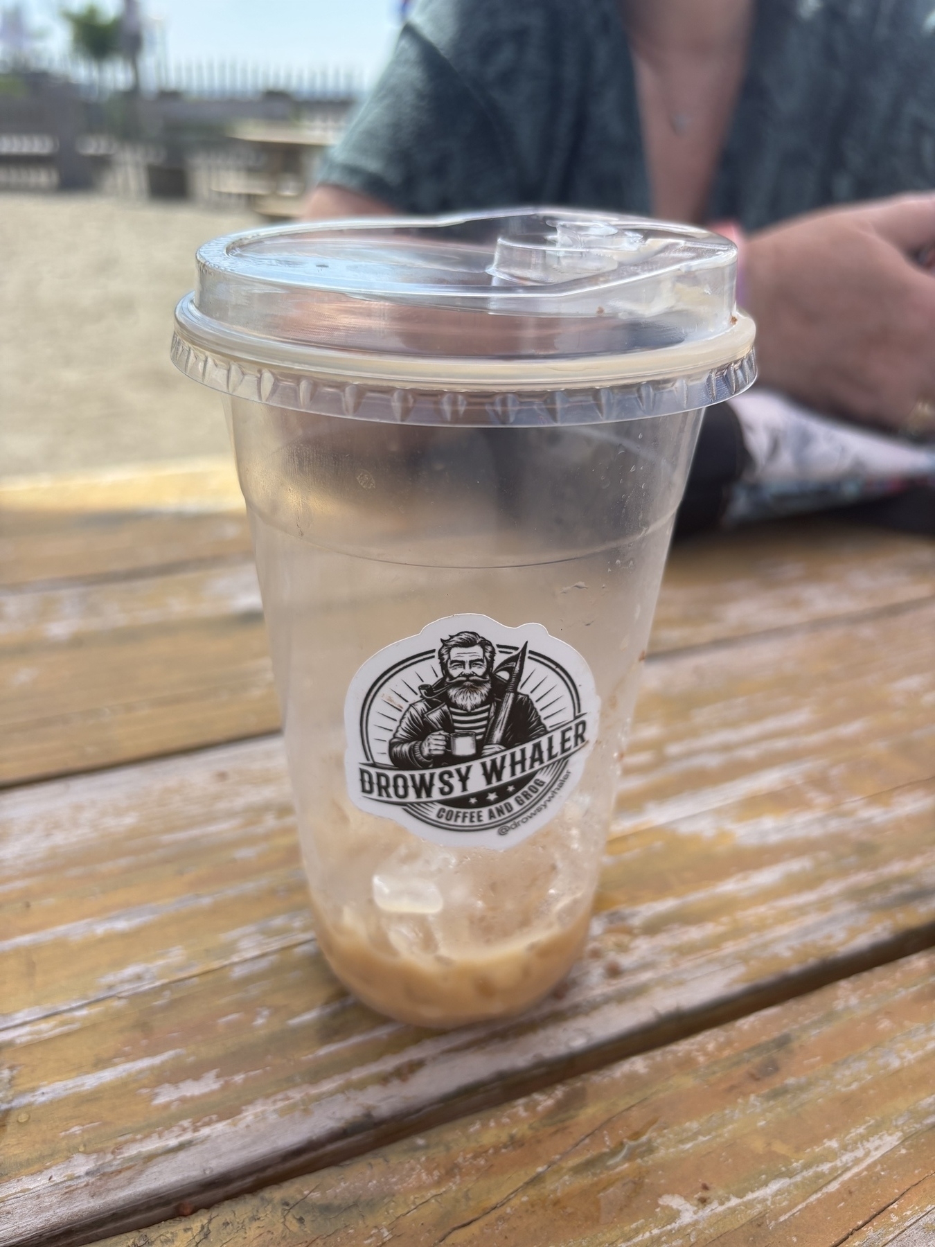 An empty cup of cold brew. A logo featuring a bearded sailor man with a harpoon and “Drowsy Whaler” “Coffee and grog”